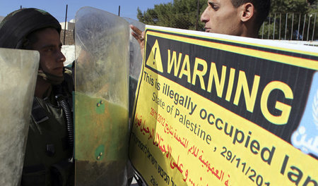 Ein Demonstrant hält einem israelischen Soldaten ein Schild gege... Ein Demonstrant hält einem israelischen Soldaten ein Schild gege...