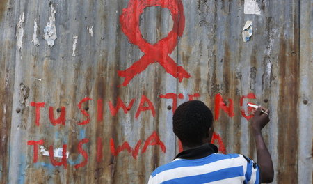 Ein junger Mann malt eine rote AIDS-Schleife auf eine Wand im Ki...