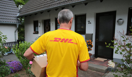 Könnte bald teuer werden: Ein DHL-Paketzusteller liefert ein Päc... Könnte bald teuer werden: Ein DHL-Paketzusteller liefert ein Päc...