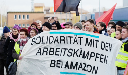 Diese Aktivisten zeigen bei einer Kundgebung vor dem Amazon-Stan...