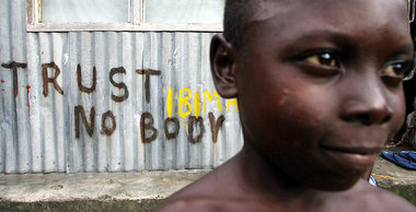 Ein nigerianischer Junge vor einem Graffito »Vertraue niemandem«...