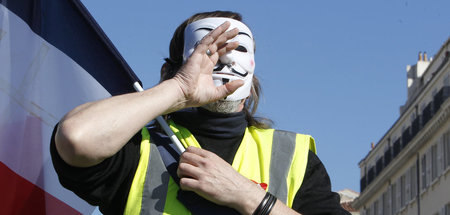 Ein maskierter Demonstrant der »Gelbwesten«-Bewegung während ein...