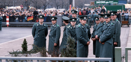 Im Hintergrund leuchtet der Westen: DDR-Grenzbeamte warten auf d...