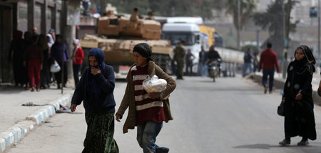 Passanten im Stadtzentrum von Afrin. Im Hintergrund Truppen der 