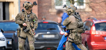 Polizisten in Kampfmontur führen einen Tatverdächtigen im Mord a...