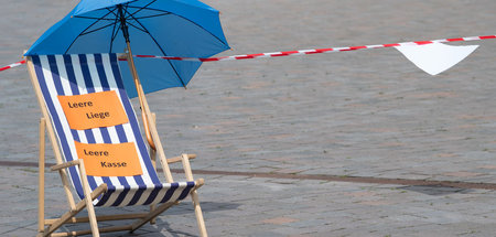 Ein Liegestuhl mit blauem Sonnenschirm und Absperrband auf dem A...