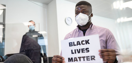 Geflüchteter aus Kamerun hält zu Beginn des Prozesses ein Schild...
