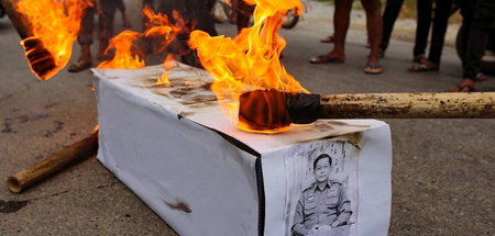 Demonstrierende verbrennen einen Pappsarg mit dem Bild von Gener...