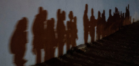 Schatten von geflüchteten Familien, die in einer Schlange vor de...