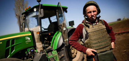 Ein ukrainischer Bauer mit Schutzweste und Helm auf einem Feld n...