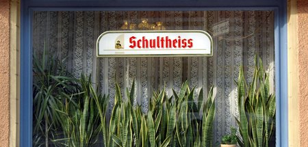 Der Kellner bringt das Bier, der Graue bedankt sich und trinkt e...