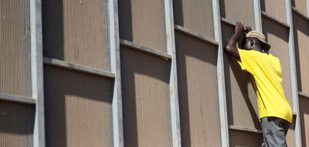 Ein Geflüchteter schaut durch den Zaun des Flüchtlingslagers auf...