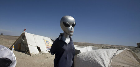 Passionierter Camper: Alien (Attrappe) steht mit Zelt in der Wüs...