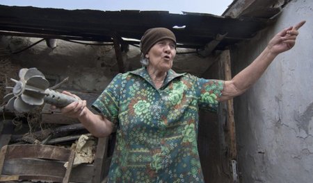 Eine Frau im Dorf Nowotroizkoje bei Donezk zeigt vor ihrem besch...
