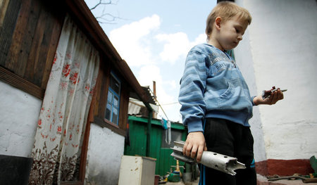 Ein Junge hebt vor einem Wohnhaus am Rand von Donezk Teile einer...
