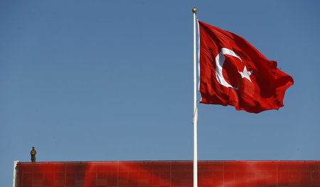 Blauer Himmel, türkische Fahne und ein bewaffneter Polizist auf ...