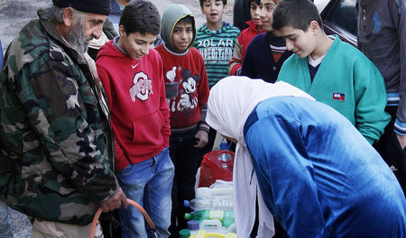 Ein Soldat der syrischen Armee bei der Verteilung von Wasser an ...