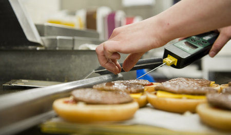 Ein Mitarbeiter prüft die Temperatur eines Hamburgers in einem B...